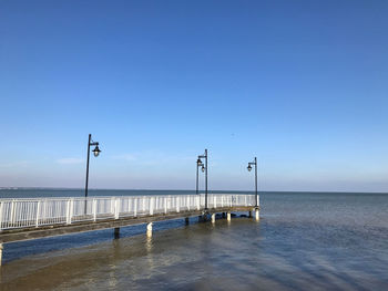 Pier on sea against clear blue sky