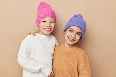 Portrait of smiling sisters wearing knit hat against beige background