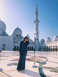 Woman standing at grand mosque against clear blue sky