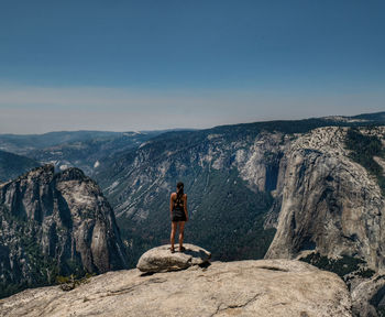 Rear view of young woman standing on mountain against sky