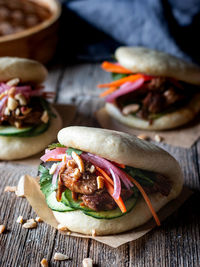 Harmful lush wheat bao buns with fresh vegetables and juicy meat on wooden table