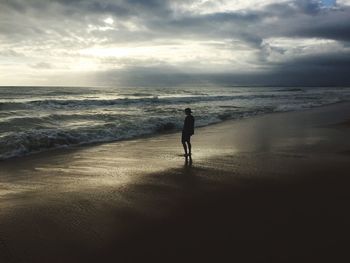 Silhouette man walking on beach against sky during sunset