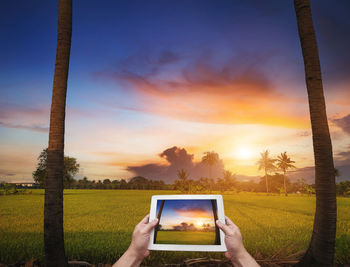 Man photographing through smart phone against sky during sunset