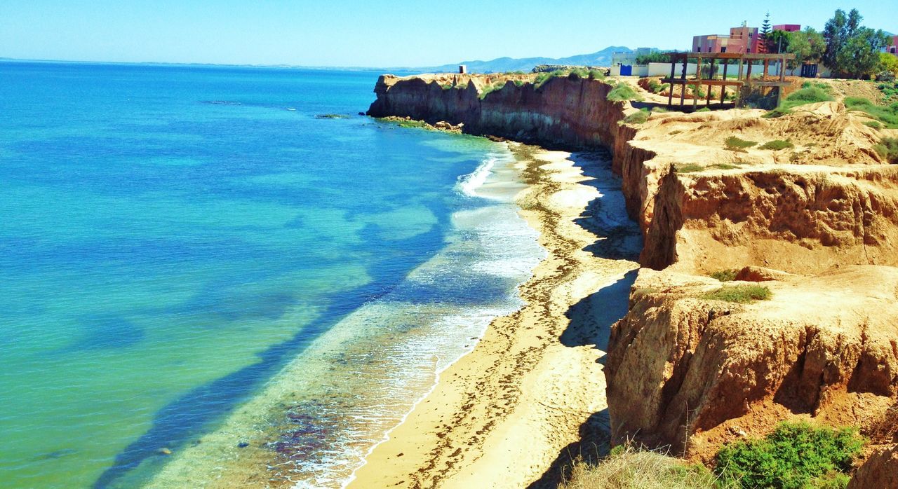 sea, water, beach, horizon over water, tranquil scene, scenics, tranquility, coastline, shore, beauty in nature, nature, rock formation, cliff, high angle view, blue, built structure, rock - object, sand, idyllic, sunlight