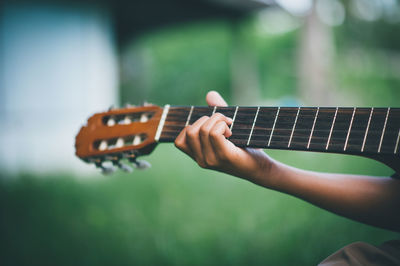 Cropped hand of person playing guitar over field