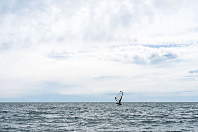 Athlete riding windsurf in the distance on blue sea against blue cloudy sky in summer, water sports