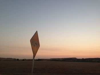 Road sign on field against clear sky during sunset