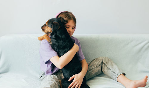 Girl embracing dog sitting on sofa at home