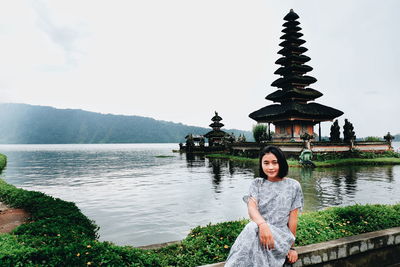 Portrait of young woman sitting against pagoda in lake