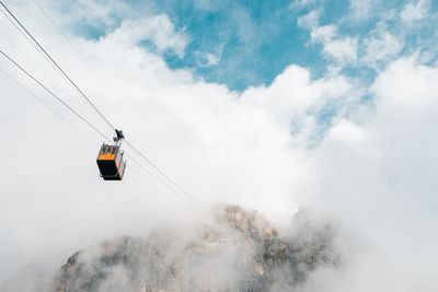 Low angle view of overhead cable cars against cloudy sky during foggy weather