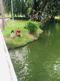 People sitting by lake against trees