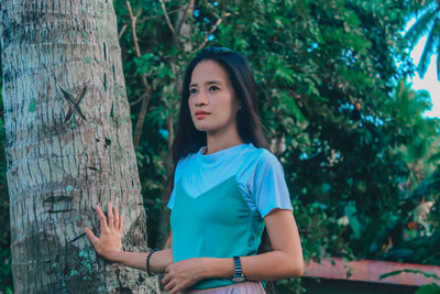 Portrait of young woman standing against tree