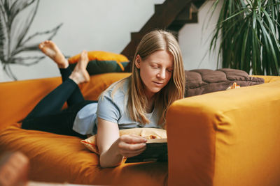 A beautiful girl is relaxing on the sofa in the living room, reading her favorite novel. 