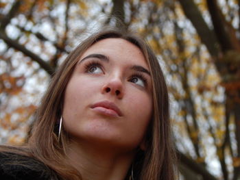 Close-up of beautiful young woman looking away against trees