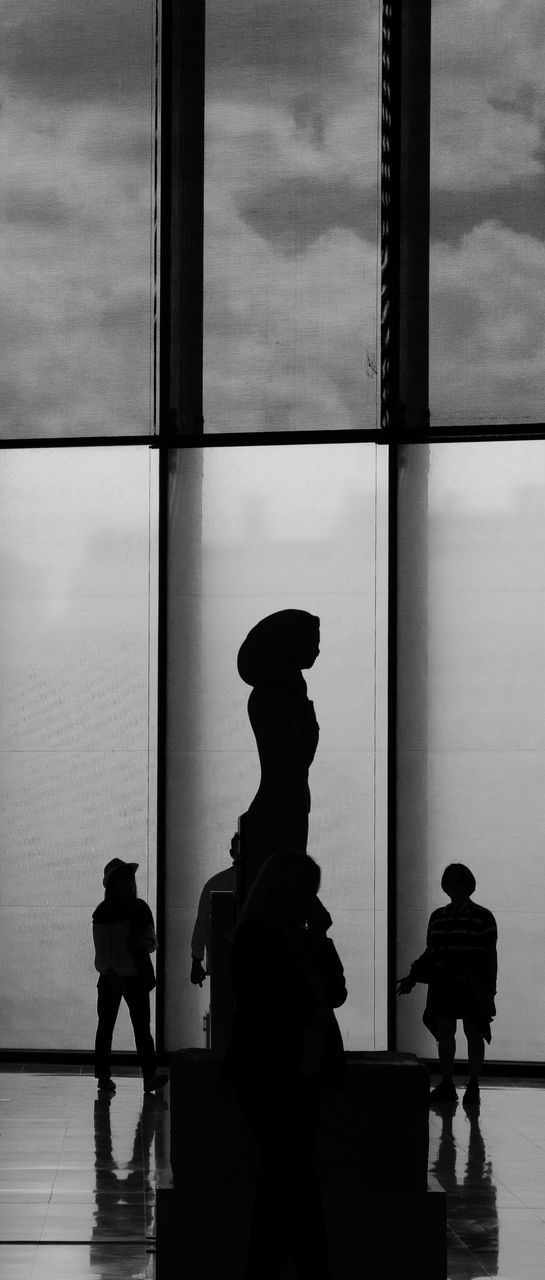 SILHOUETTE MAN STANDING BY STATUE AGAINST WINDOW IN CITY