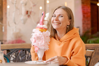 Happy woman eating sweet dessert in form pink flamingo in restaurant, woman