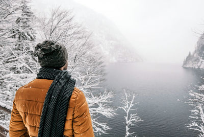 Rear view of man standing on viewpoint over lake in winter, snow, nature, hiking.