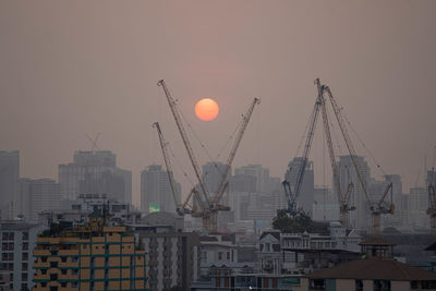 Cranes in city against sky during sunset