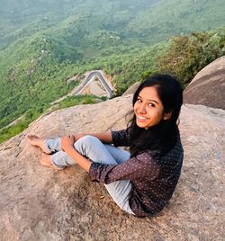 High angle view portrait of smiling woman sitting on mountain