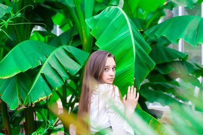 Portrait of young woman standing by banana leaf outdoors