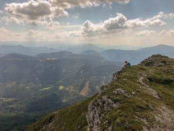 Scenic view of mountains with woman sitting on grass against sky