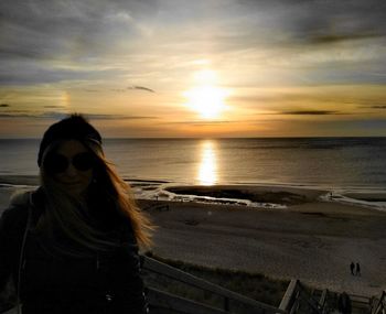 Woman standing on beach against sky during sunset