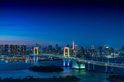 Illuminated bridge over river against blue sky at night