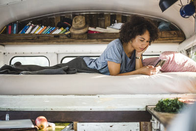 Young afro woman surfing through mobile phone while lying on bed in motor home