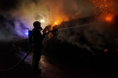 Silhouette man standing by fire at night