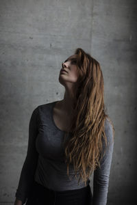 Beautiful young woman looking up while standing against wall