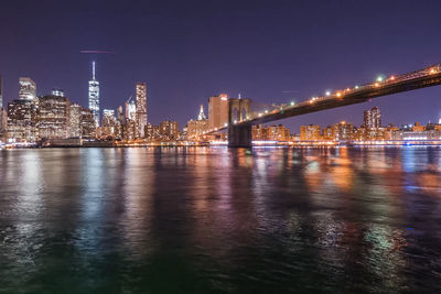 Illuminated buildings by river against sky at night