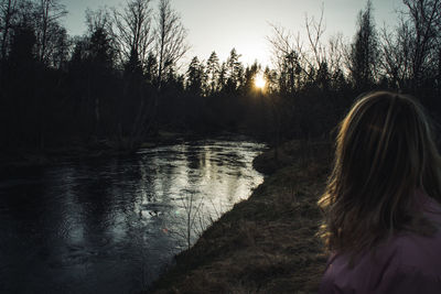 Rear view of woman in lake against sky during sunset