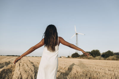 Woman with arms outstretched standing on wheat field in front of sky