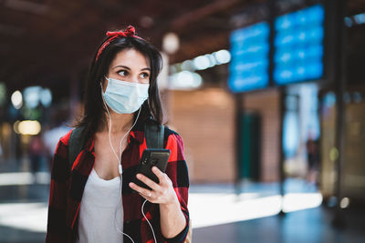 Young woman wearing mask looking away while standing at airport