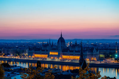 Hungarian parliament building by danube river against sky at dusk