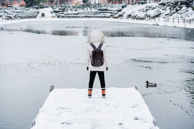 Wide angle view of back view of backpacker woman standing in front of frozen lake in city