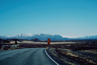 Road leading towards snowcapped mountains against clear blue sky