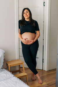 Happy pregnant woman stands at home.