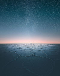 Distant man standing on scenic salt flat against starry sky at night
