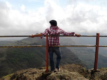 Rear view of man standing by sea against cloudy sky