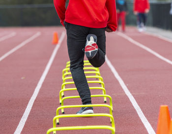 Rear view of a high school track runner running the wicket drill with banana hurdles on a track.