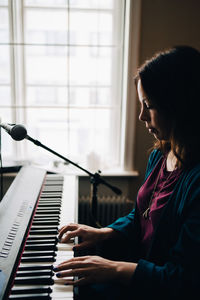 Side view of woman playing piano by window at studio