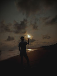 Rear view of silhouette man standing on beach during sunset