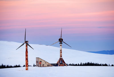 Windmills on snow covered landscape against sky during sunset