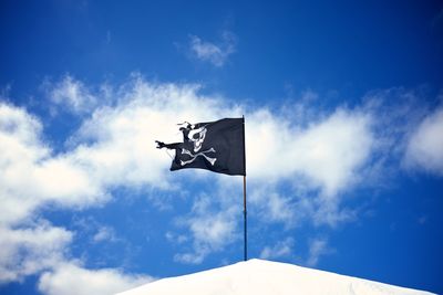 Low angle view of torn pirate flag against sky