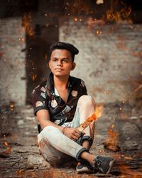 Digital composite image of young man sitting amidst fire
