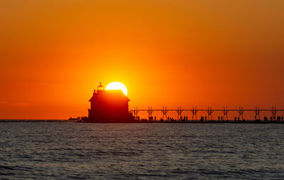 Grand haven, michigan, catwalk and lighthouse in silhouette against bright orange sky and sunset