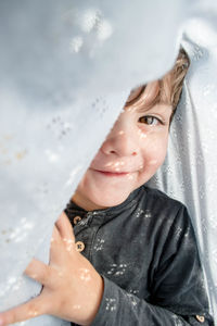 Portrait of boy smiling amidst white curtain