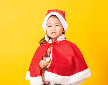 Portrait of cute girl wearing santa costume against yellow background