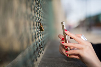 Cropped hands of woman photographing padlock on fence